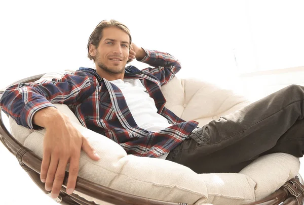 Ernster Kerl sitzt in einem großen bequemen Stuhl. Seitenansicht. — Stockfoto