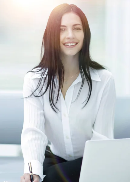 Erfolgreiche junge Frau sitzt an einem Schreibtisch vor verschwommenem Hintergrund. — Stockfoto