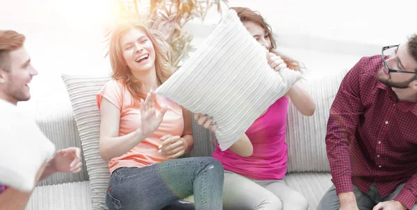 Amigos alegres brincando com os travesseiros sentados no sofá — Fotografia de Stock