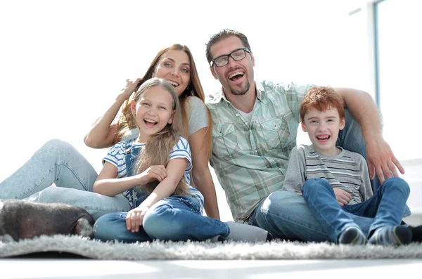 Família alegre sentado no tapete na nova sala de estar — Fotografia de Stock