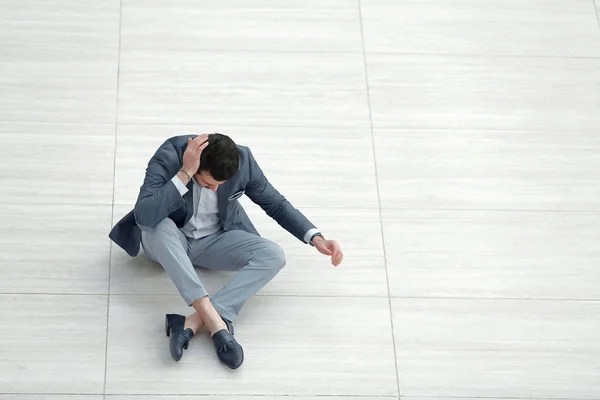 Frustrierter junger Geschäftsmann sitzt auf dem Boden und blickt nach unten. — Stockfoto