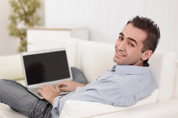 Schöner Mann benutzt einen Laptop, schaut in die Kamera und lächelt — Stockfoto