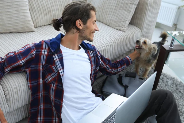 Elegante giovane uomo accarezzando il suo animale domestico e lavorando sul computer portatile — Foto Stock