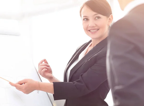 Lächelnde Geschäftsfrau zeigt Kollegen Informationen auf dem Flipchart. — Stockfoto