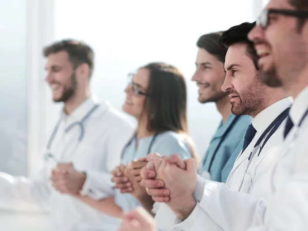 Doctors sit in a row and hold hands of each other — Stock Photo, Image