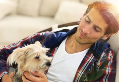 yakışıklı olan büyük bir koltukta otururken köpeğini okşayarak.