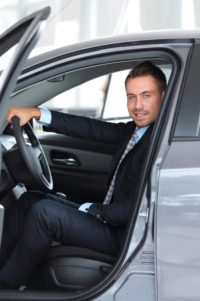 Hombre de negocios sentado al volante de un coche, en el estacionamiento en el concesionario de automóviles — Foto de Stock