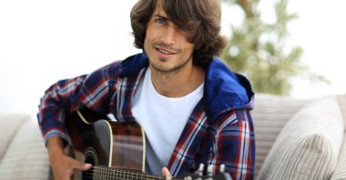 modern adam kanepede oturan gitar çalmak. bir yaşam tarzı kavramı