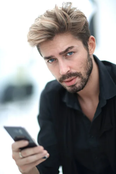 Ένα κομψό γενειοφόρος άνδρας κάθεται και χρησιμοποιεί ένα smartphone. — Φωτογραφία Αρχείου