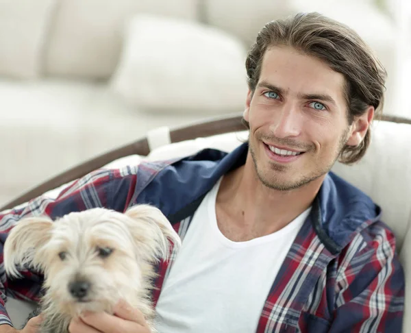 Stilig kille strök hans hund när man sitter i en stor fåtölj. — Stockfoto