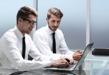 Genç ofis çalışanı gülümsüyor, iş arkadaşları arka grupta çalışıyor.