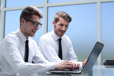 Genç ofis çalışanı gülümsüyor, iş arkadaşları arka grupta çalışıyor.