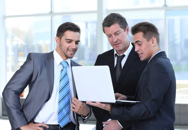 Affärskollegor tittar på en bärbar dator, stående i lobbyn på kontoret. — Stockfoto