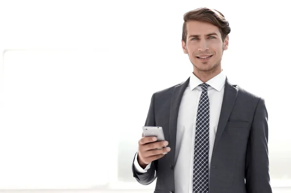 Hombre de negocios con teléfono inteligente de pie en una oficina brillante — Foto de Stock