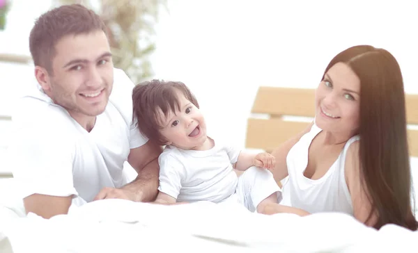 Feliz familia joven con un bebé acostado en la cama y sonriendo —  Fotos de Stock