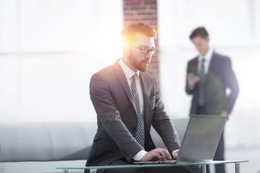 Yakışıklı iş adamı ofiste dizüstü bilgisayarla çalışıyor.