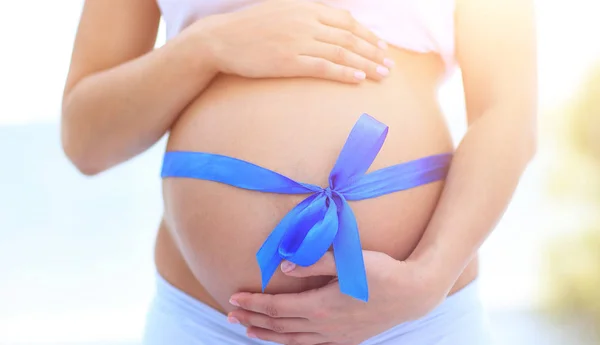 Крупним планом вагітна жінка зав'язує на животі блакитну стрічку — стокове фото