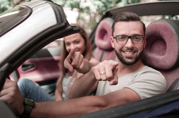 Casal amoroso em um carro conversível apontando para você — Fotografia de Stock