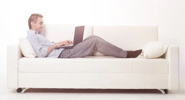 Man som arbetar på laptop liggande på en soffa — Stockfoto