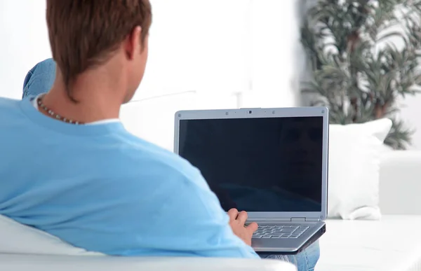 Giovane uomo casuale che lavora sul computer portatile mentre sdraiato sul divano . — Foto Stock