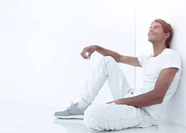 Stock image dreamy young man sitting beside a white wall.