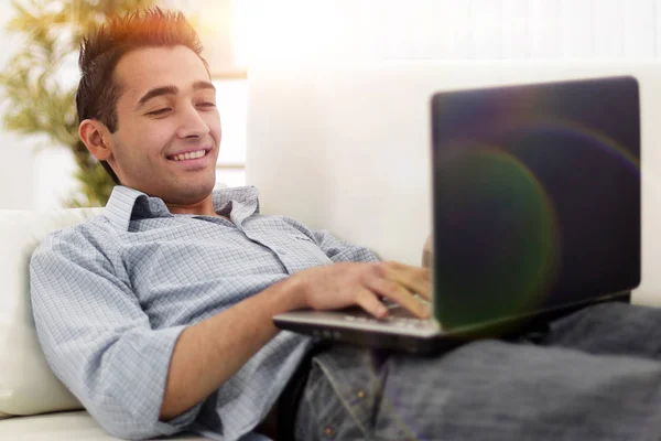 Jovem, homem bonito usando laptop sentado no sofá — Fotografia de Stock