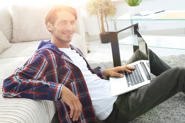 소파 근처 바닥에 앉아 노트북으로 젊은 남자를 웃 고 — 스톡 사진