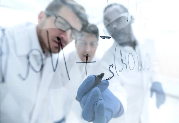 Close up. a group of scientists recording the formula on a glass — стоковое фото