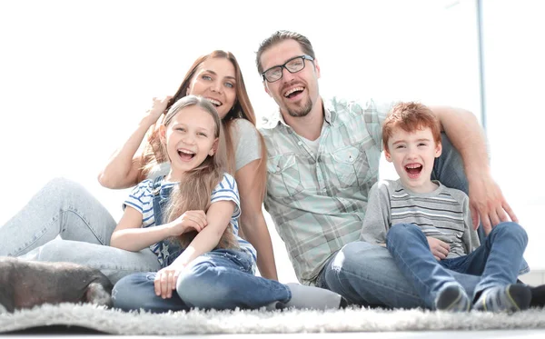 Vrolijke familie zittend op het tapijt in de nieuwe woonkamer — Stockfoto
