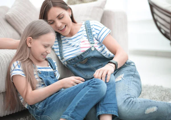 Mãe com uma pequena filha usando um smartphone sentado na nova sala de estar — Fotografia de Stock