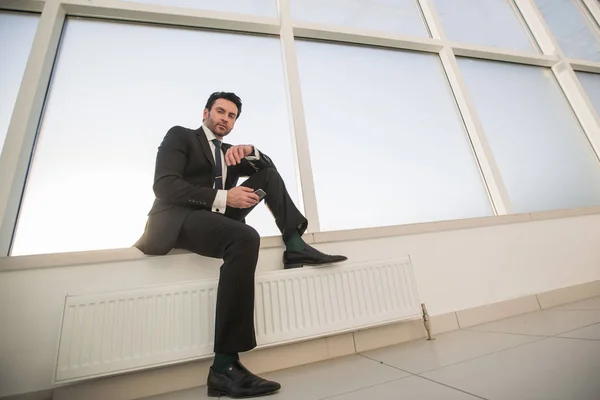 Uomo d'affari fiducioso con uno smartphone seduto nel corridoio dell'ufficio — Foto Stock