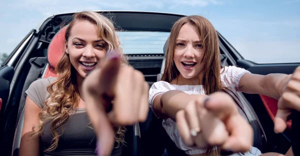 Дві щасливі подружки сидять в машині і вказують на вас — стокове фото