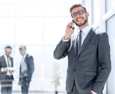 Banka ofisinin yanında cep telefonu olan bir işadamı duruyor.