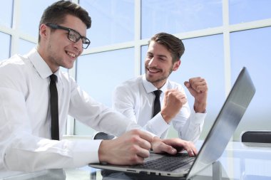 Genç ofis çalışanı gülümsüyor, iş arkadaşları arka grupta çalışıyor.