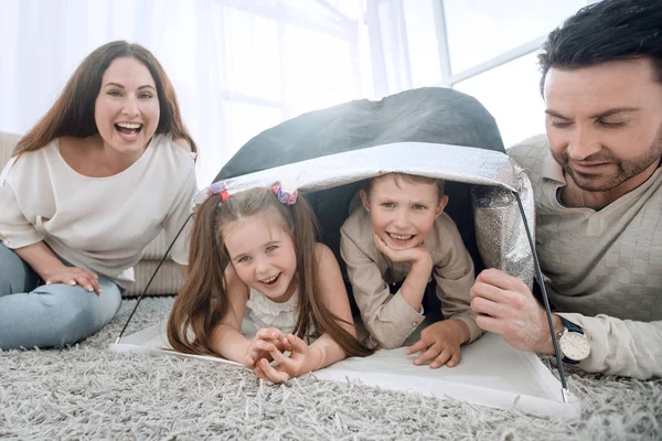 Pais felizes brincam com crianças em uma tenda na sala de estar — Fotografia de Stock