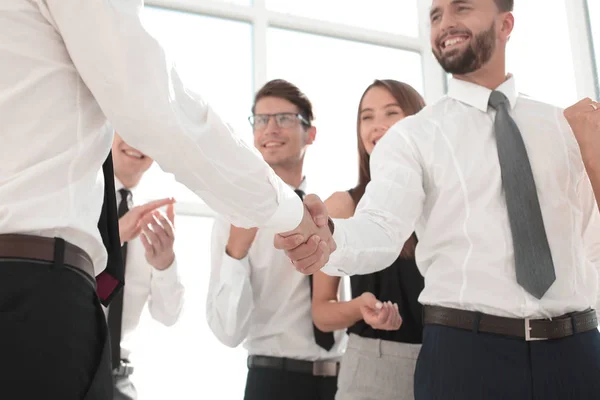 In de foreground.handshake mensen uit het bedrijfsleven in het kantoor. — Stockfoto