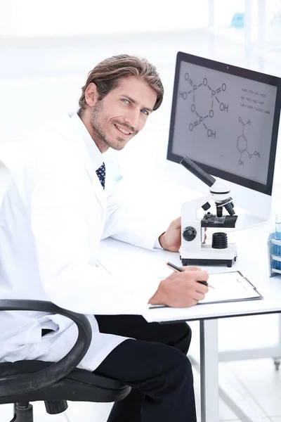 Operaio di laboratorio seduto al tavolo con microscopio — Foto Stock