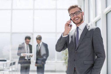 Banka ofisinin yanında cep telefonu olan bir işadamı duruyor.