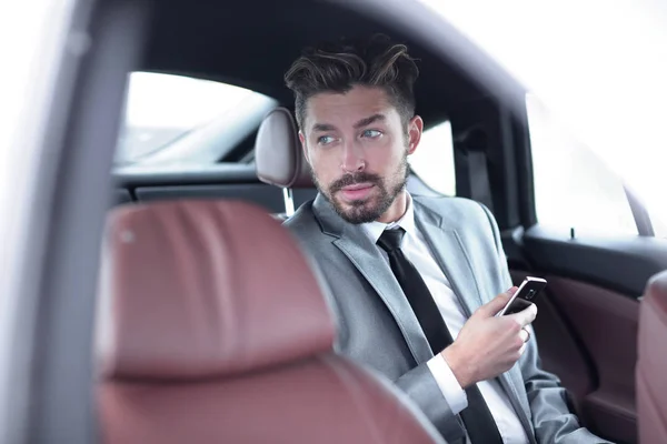 Homme en costume assis en voiture et lisant des messages sur smartphone — Photo