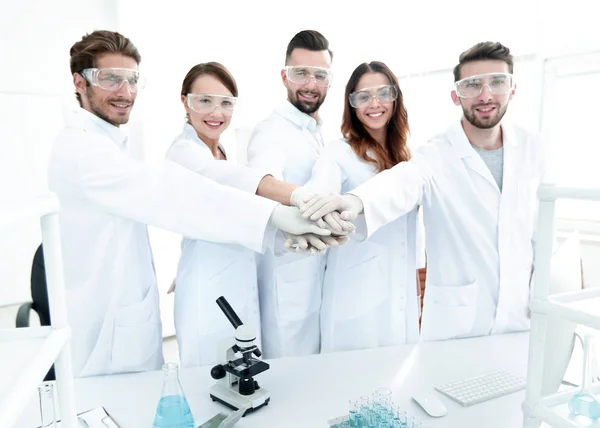 Erfolgreiches Team junger Wissenschaftler mit zusammengeklammerten Händen. — Stockfoto