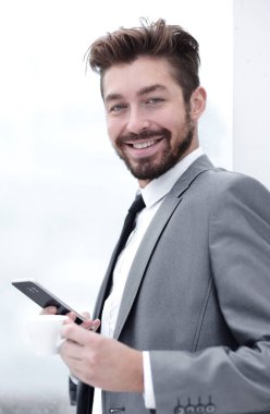 Takım elbiseli şık adam telefonla bilgi okuyor.