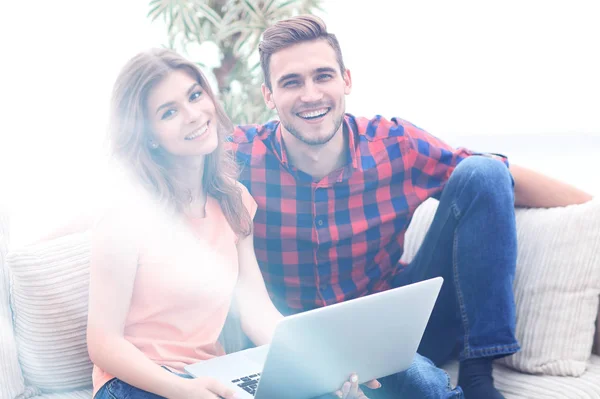 Jovem casal de alunos usa um laptop sentado no sofá — Fotografia de Stock