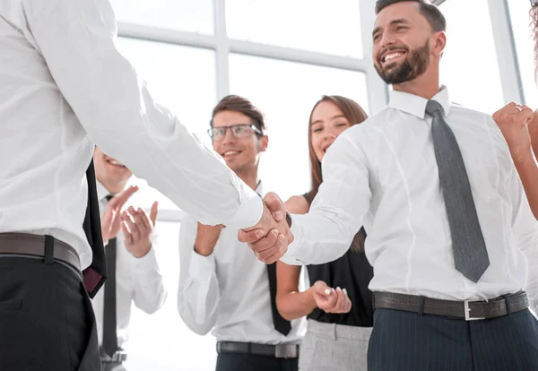 In de foreground.handshake mensen uit het bedrijfsleven in het kantoor. — Stockfoto