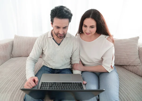 Pareja casada sentada en el sofá y mirando la pantalla del ordenador portátil — Foto de Stock