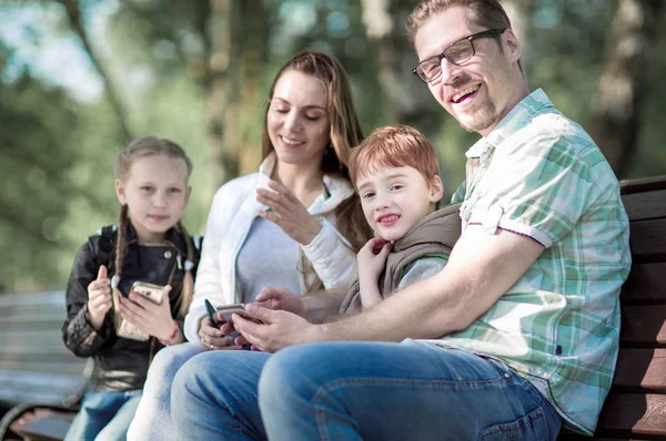 Família feliz sentado no banco no parque de verão — Fotografia de Stock