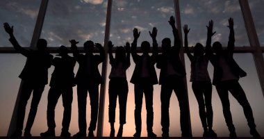 Bir grup iş adamının silueti ellerini kaldırıyor.