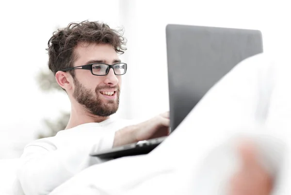 Χαμογελαστός άνθρωπος που χρησιμοποιούν φορητό υπολογιστή ξαπλωμένος στο κρεβάτι — Φωτογραφία Αρχείου