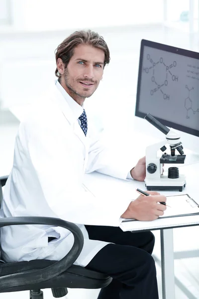 Laboratory worker sitting by table with microscope