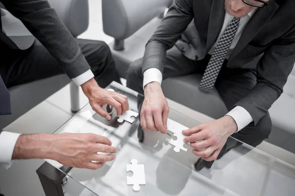 Close up.business partners putting together a puzzle, sitting at office Desk — стоковое фото