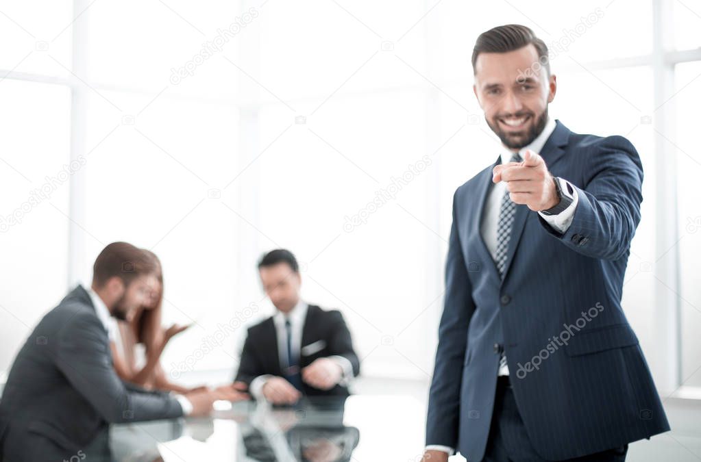 smiling businessman standing in the office and pointing at you